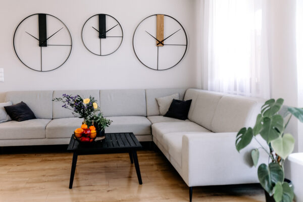 Duże, loftowe zegary ścienne SC96 nad szarą sofą w nowoczesnym salonie – modele Classic i Elegance